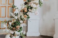 a jaw-dropping wedding backdrop of blush, white and peachy blooms, greenery and moss on the floor gives a garden feel to the space