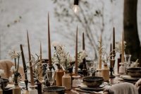 a lovely boho wedding reception with white blooms and greenery, with candles of various colors, with bulbs hanging down and some dried leaves