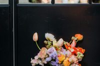a lovely colorful wedding bouquet of blush tulips, lilac, peachy, orange and red blooms of various kinds and a tulle ribbon