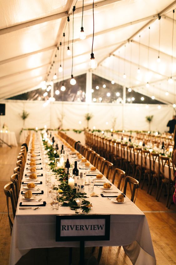 a lovely neutral wedding reception space with greenery and candles, with bulbs hanging over the tables is a beautiful idea to rock