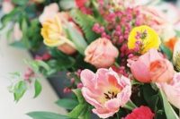 a lovely wedding centerpiece of light pink and yellow tulips, greenery, red blooms and berries is amazing for a colorful wedding