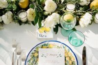 a lovely wedding tablescape with a greenery, white bloom and lemon table runner, candles and a lemon printed plate, green glasses