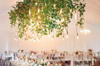 a lush and bold wedding installation of a wooden grid, greenery and bulbs hanging down is a beautiful decor idea for a modern wedding