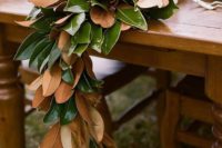 a lush magnolia leaf wedding table garland with candles on an uncovered table is a chic and bold idea