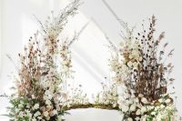 a lush wedding backdrop of white and blush blooms, dried herbs and leaves, greenery and triangle arches over the space