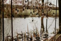 a metal frame over the table decorated with dried leaves and bulbs down is a beautiful boho fall wedding idea
