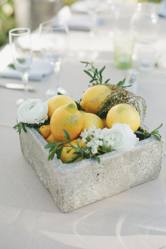 a modern wedding centerpiece of a concrete box, white blooms and greenery and lemons is a catchy and out of the box idea