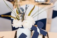 a nautical wedding centerpiece of a wood slice, a navy anchor, white blooms and berries, candles and a table number