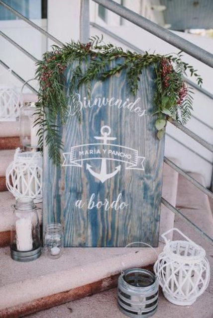 a nautical wedding sign in blue, with greenery, berries and candle lanterns around is a stylish idea for a seaside wedding