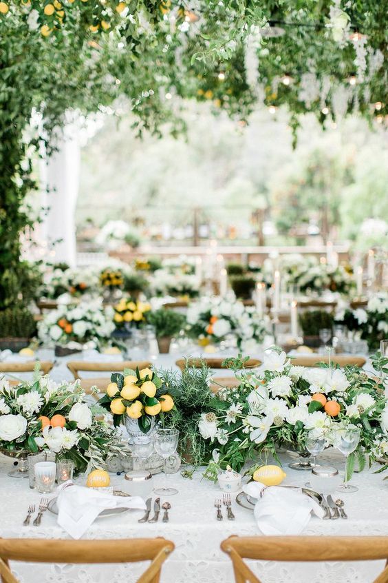 a neutral summer wedding table setting with white blooms, greenery, oranges and lemons and lemons on the table that add color and interest