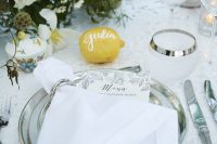 a neutral wedding tablescape with a lace tablecloth, neutral plates, greenery, white blooms and a lemon as a place card is awesome