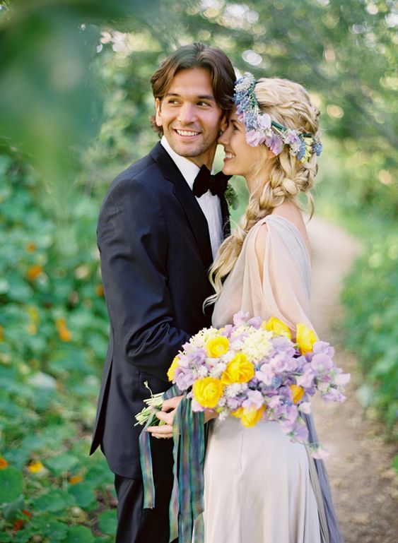 a pretty boho spring bridal look with a lilac wedding dress, a lilac and blue flower crown, a matching wedding bouquet with some yellow ranunculus