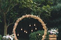a round wedding arch covered with pampas grass and bulbs, with pastel blooms and greenery and candles around