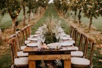 a rustic outdoor wedding reception space with a wooden dining table, fruits and berries on the table, greenery and grasses for centerpieces and bulbs over the space