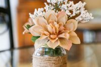 a rustic wedding centerpiece of a jar wrapped with twine, a burlap bloom and a branch of faxu baby’s breath is cool