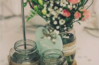 a rustic wedding centerpiece of a wood slice, jars with twine, candles, an arrangement of baby’s breath and pink blooms