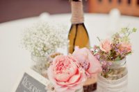 a rustic wedding centerpiece of wood slices, jars with lace, pink roses and baby’s breath plus a chalkboard sign