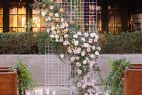 a simple modern wedding backdrop of mesh, white, pink and peachy blooms and foliage, candles on the ground is refined
