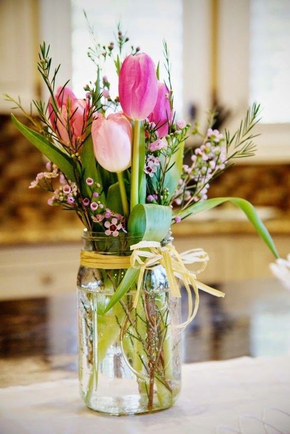 a simple rustic wedding centerpiece of hot pink and light pink tulips, waxflower and greenery in a jar is a gorgeous idea for a wedding with touches of pink