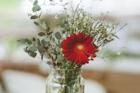 a small and simple wedding centerpiece of greenery, baby’s breath and a red gerberas in a jar for a rustic wedding