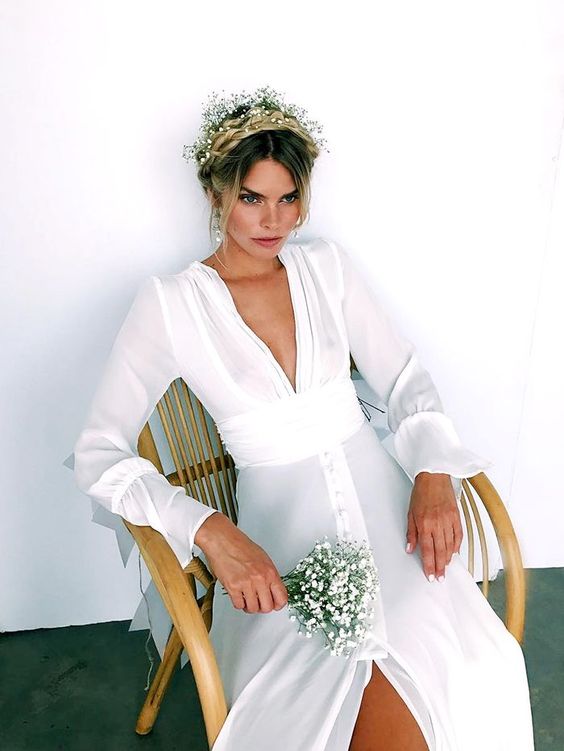 a spring boho bridal look with an updo with a braided halo, with baby's breath tucked in, a simple plain wedding dress with a plunging neckline and a small wedding bouquet