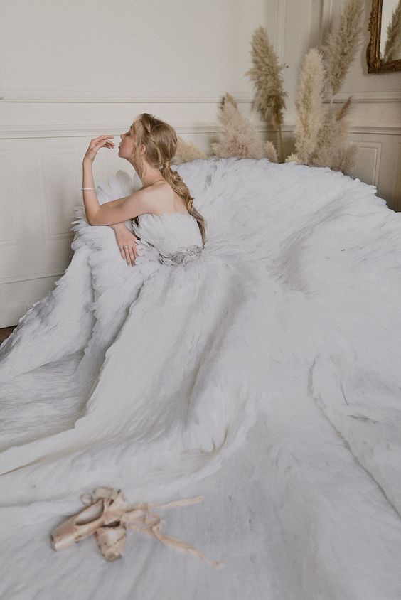 a strapless A-line wedding dress fully covered with feathers, with an embellished sash and a train