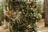 a super lush and wild botanical wedding backdrop of blush, burgundy and deep purple blooms, foliage and fronds for a boho wedding