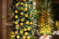 a tall wedding centerpiece of greenery and small lemons is a creative decor idea for a summer wedding with a formal feel