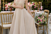 a tan wedding dress with a fully embellished bodice with no sleeves and a pleated maxi skirt with a train