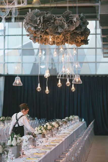 a unique wedding reception with white blooms and candles on the table and a pale foliage and bulbs over the table for a bolder look