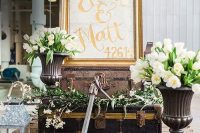 a vintage nautical wedding decor with rope, a large real anchor, candle lanterns, suitcases, white blooms and greenery and a sign