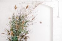 a wedding altar made of greenery and dried grasses is a lovely and chic idea for a modern wedding with a botanical feel