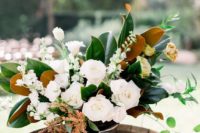 a wedding centerpiece is made of magnolia leaves, white blooms and herbs is a chic and dimensional idea