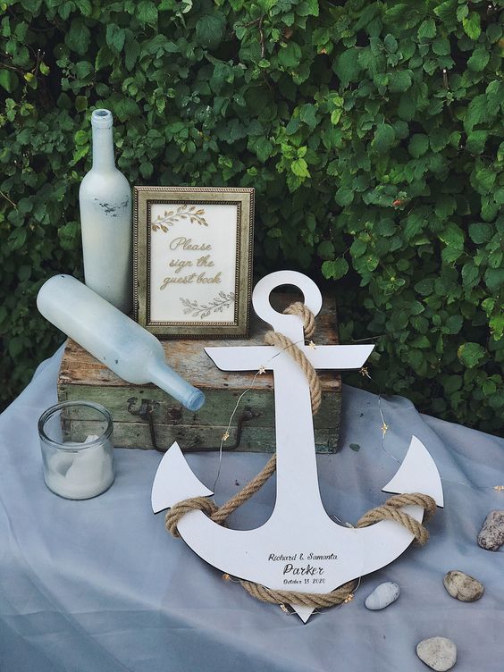 a wedding guest book made of an anchor, with bottles and candles and pebbles plus lights is a cool idea for a nautical wedding