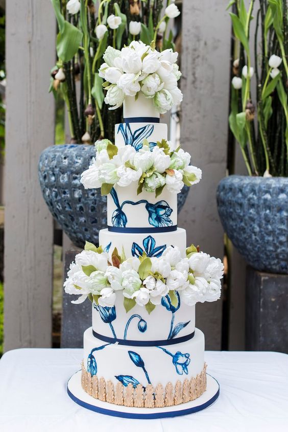 a whimsical wedding cake with painted blue flowers and fresh white tulips is a fantastic idea for a wedding
