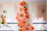 a white wedding cake decorated with orange sugar blooms and pink gerberas is amazing for a bright wedding