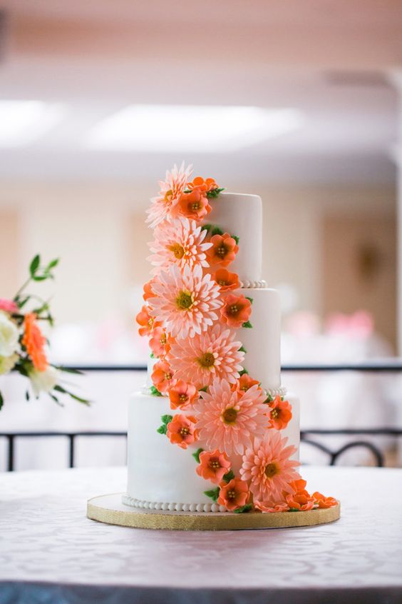 a white wedding cake decorated with orange sugar blooms and pink gerberas is amazing for a bright wedding