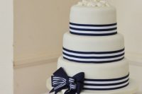a white wedding cake with navy and white stripes and a bow, with seashells and wooden anchor cake toppers is a lovely idea for a nautical wedding
