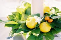 an easy and lovely wedding centerpiece of foliage, lemons and kumquats and a pillar candle in the center is awesome for summer