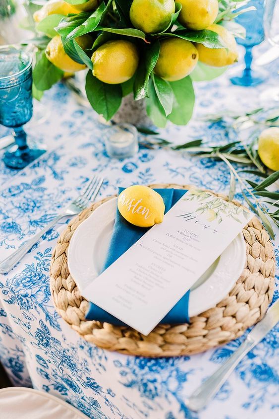 an extra bold wedding tablescape with a blue floral print tablecloth, a lemon wedding centerpiece, chunky woven placemats and blue napkins and glasses