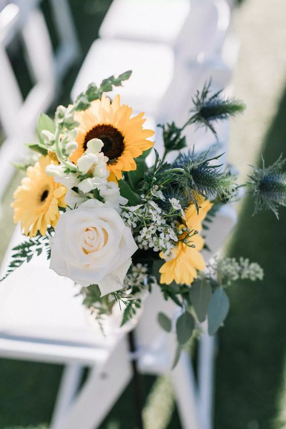 bold aisle chair decor with yellow gerberas, sunflowers, white roses and waxflower, greenery and thistles