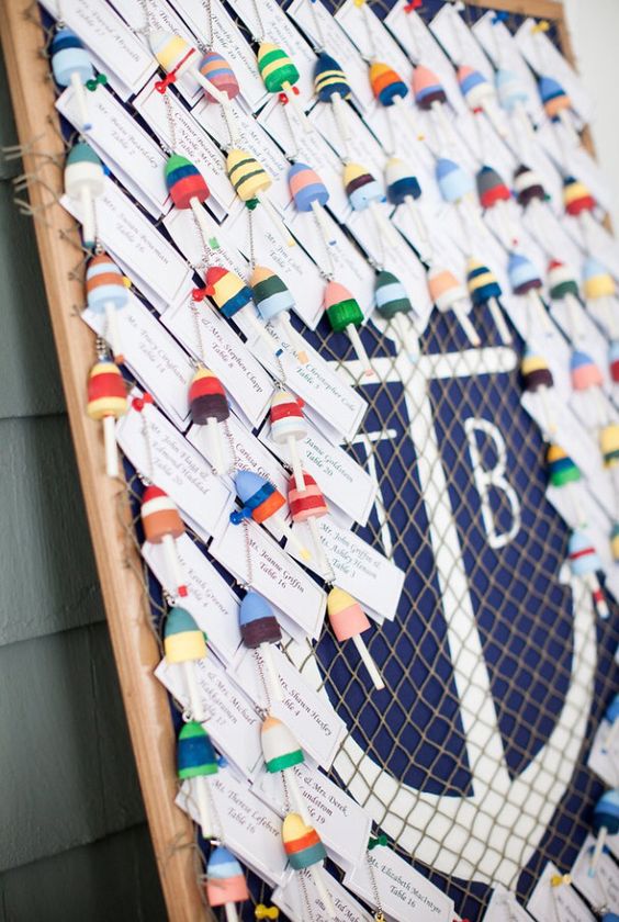 hand painted mini buoys for guests to have as ornament and keychain keepsakes hung on a painted cork board with a large anchor