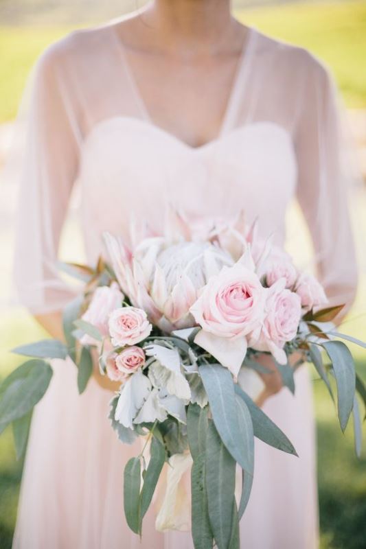 a subtle wedding bouquet of light pink roses and a king protea plus greenery is a gorgeous statement for a spring or summer wedding