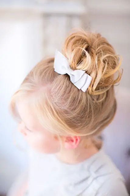 a top knot with curls and a white bow is a very lovely idea that will match many flower girl looks