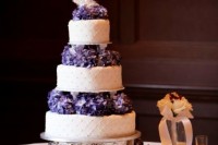 a chic white patterned wedding cake with purple flowers between the tiers is super bright and cool