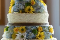 a rustic wedding cake with textural tiers, bright yellow and blue blooms between the tiers and cute bird toppers
