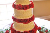 a white patterned wedding cake with bright red blooms between the tiers is super bold and romantic