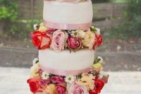a bright and chic white wedding cake with pink ribbons and colorful flowers between the tiers is very catchy
