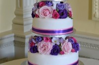 a colorful wedding cake with white tiers and purple and pink blooms between the tiers is wow