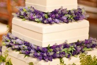 a bold square wedding cake with purple and lilac blooms plus greenery between the tiers